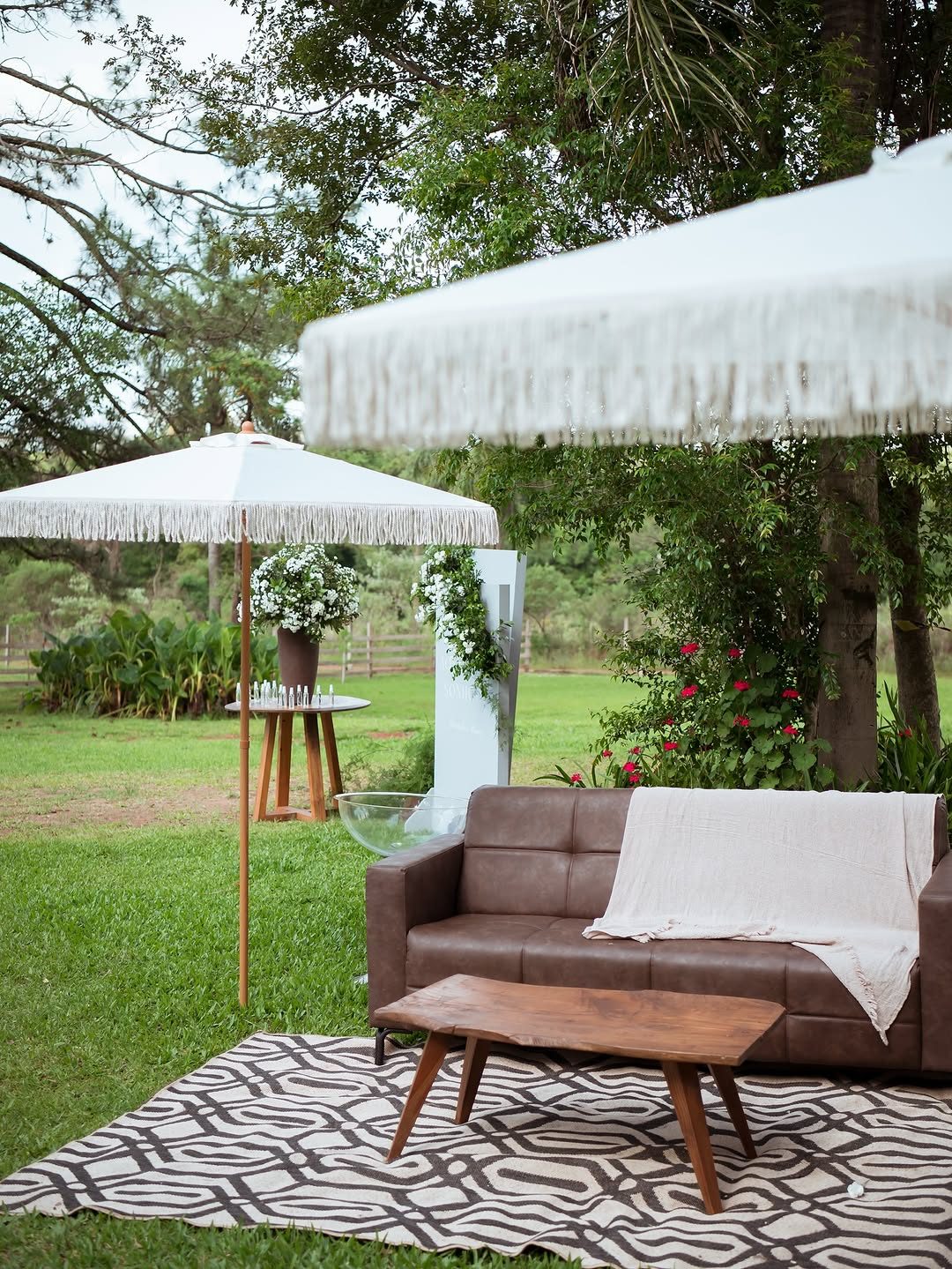 Lounge com sofá, mesa e ombrelones montado no gramado para um casamento