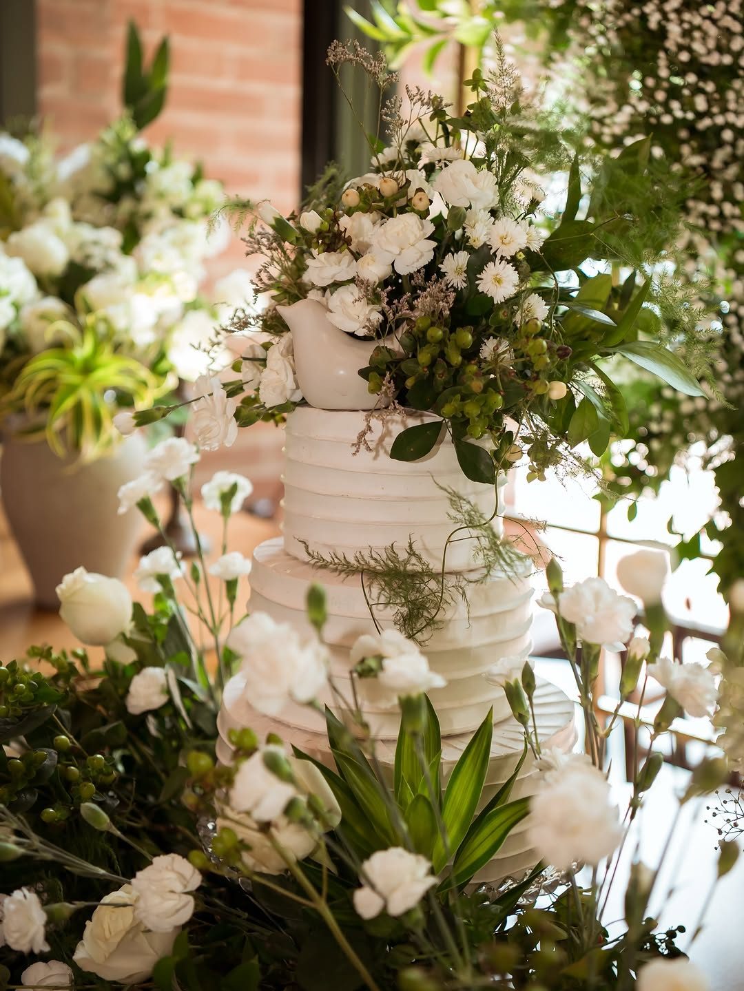 Bolo branco cercado por flores e folhagens na decoração de casamento
